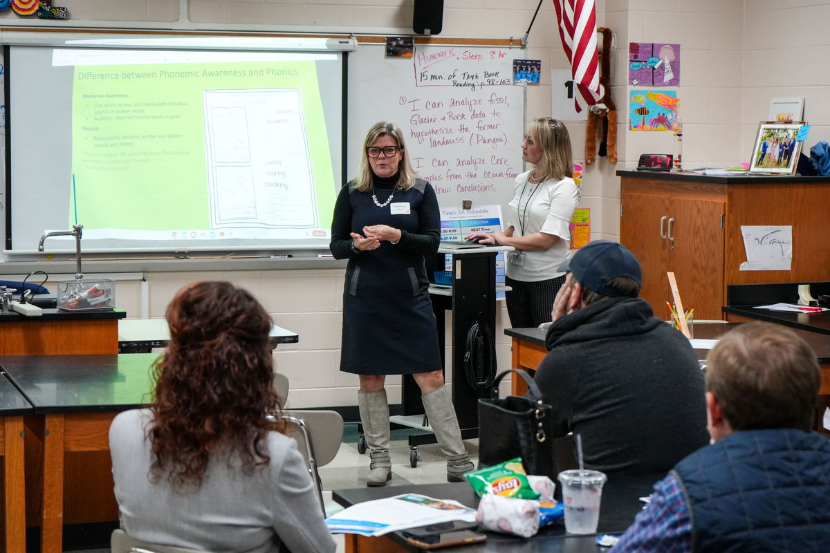 Two presenters address a room of parents